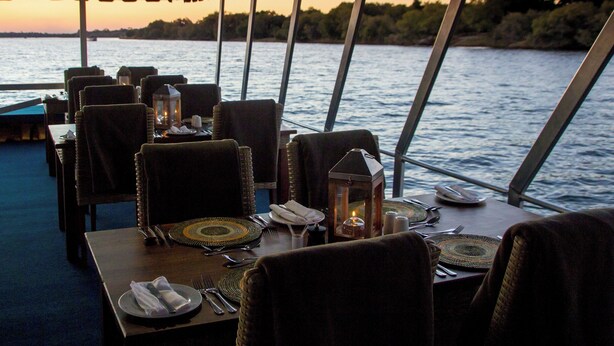 A dining area with tables set for two, equipped with tableware and lanterns, overlooking a body of water.