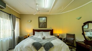 Una habitación de hotel con una cama grande, lámparas de noche, un ventilador de techo, un cuadro en la pared y una silla de madera.