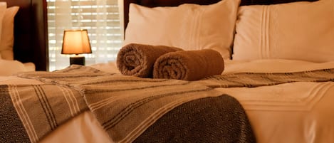 A neatly made bed with a patterned blanket, a rolled towel, and a bedside lamp.