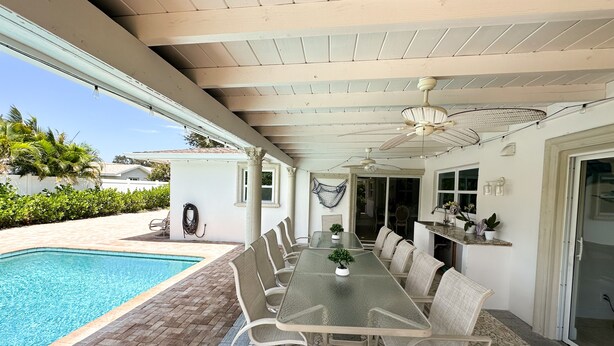 A covered outdoor dining area with a pool, wicker chairs, and a table.