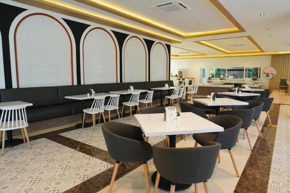 A modern restaurant with a long counter, white tables, and black chairs. - M CASA HOTEL PATTAYA (Pattaya)