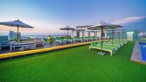 A rooftop pool area with green artificial grass, lounge chairs, and umbrellas. - M CASA HOTEL PATTAYA (Pattaya)