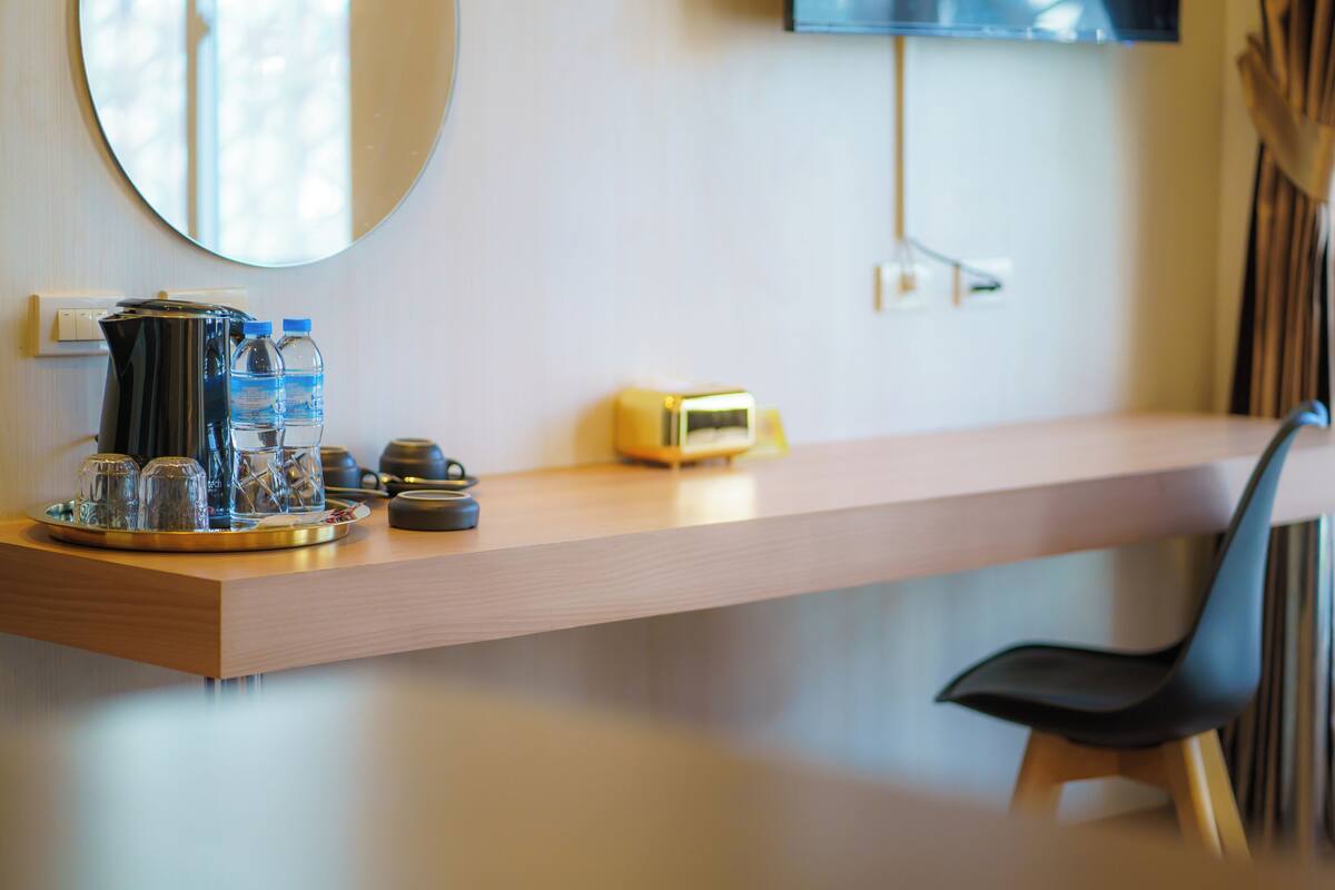 A hotel reception desk with a coffee maker, two water bottles, a clock, and a chair.