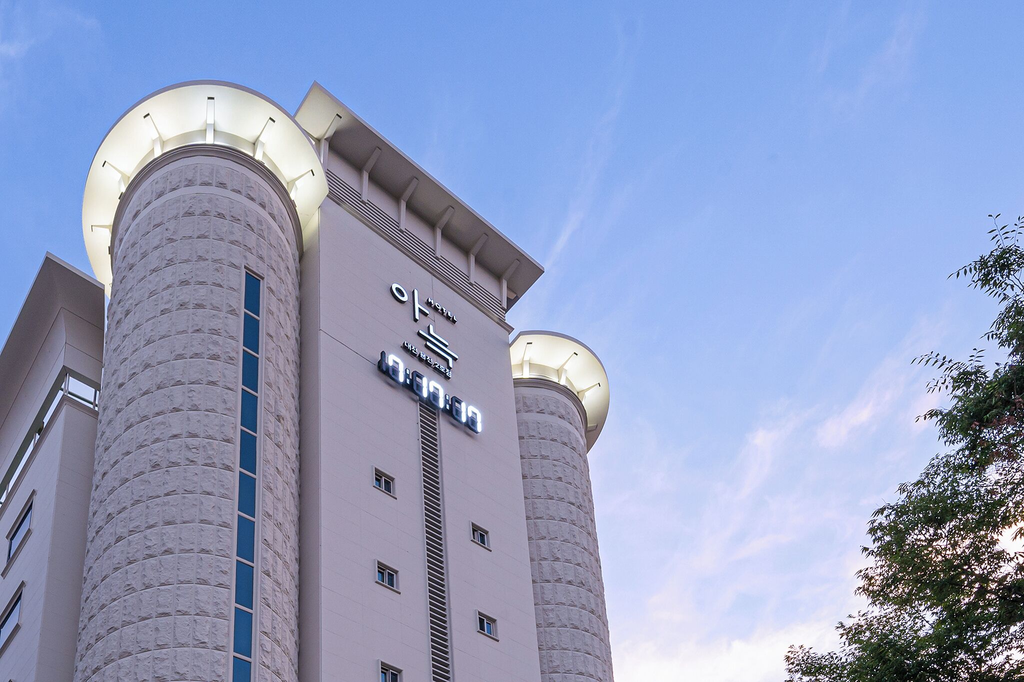 A modern hotel with two cylindrical towers, a prominent sign, and a clear sky.