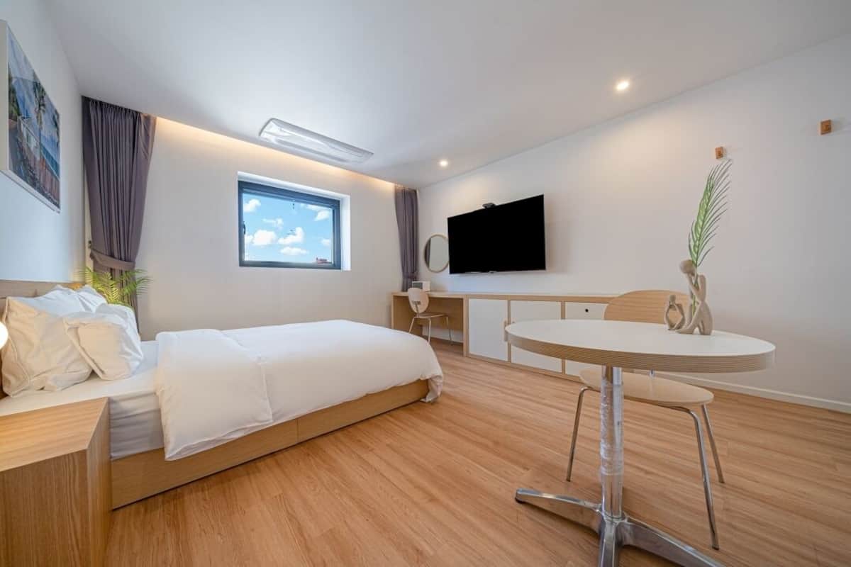 A modern hotel room with a bed, a desk, a chair, a TV, and a window.