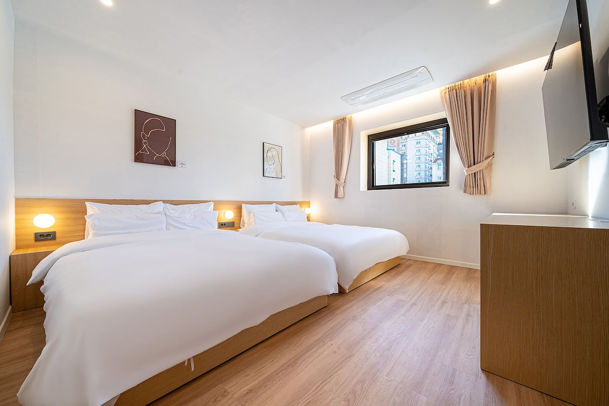 A hotel room with two beds, a desk, a TV, and artwork on the walls.