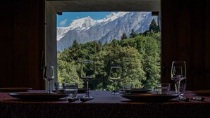 Una mesa de comedor con copas de vino y platos, con el paisaje de montañas al fondo visible a través de un arco abierto.