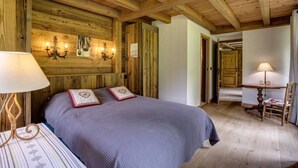 Una habitación de madera con una cama, una mesa y una silla. Hay apliques de pared y una lámpara de araña.