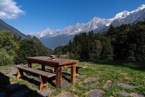 Een houten picknicktafel met bankjes in een bergachtig gebied, met besneeuwde toppen op de achtergrond.