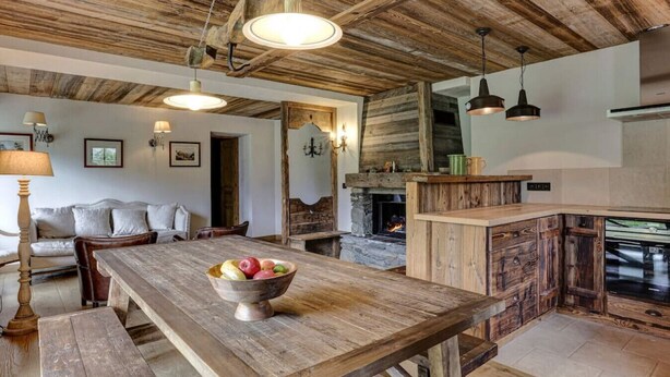 Eine rustikale Küche mit Holztisch, Kamin aus Stein und hängenden Pendelleuchten.
