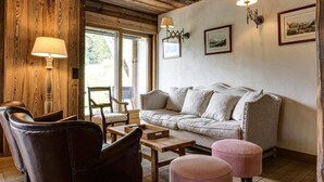 Ein gemütliches Wohnzimmer mit Ledersessel, Sofa und Couchtisch. An den Wänden sind zwei Wandlampen und gerahmte Bilder angebracht.