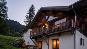 Eine Holzhütte mit Balkon, Steinfundament und Blick auf den umliegenden Wald.
