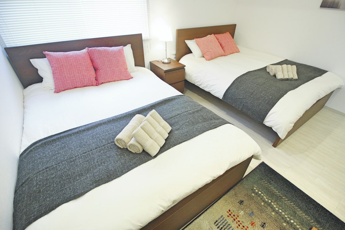 Dos camas individuales con cabeceros de madera, ropa de cama blanca y almohadas rosas y rojas. Cada cama tiene una mesita de noche con una lámpara.