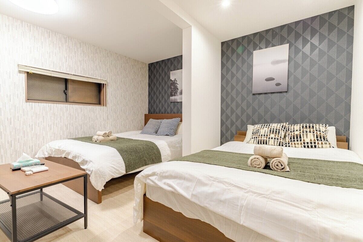 Habitación de hotel con dos camas, una mesita y una ventana.