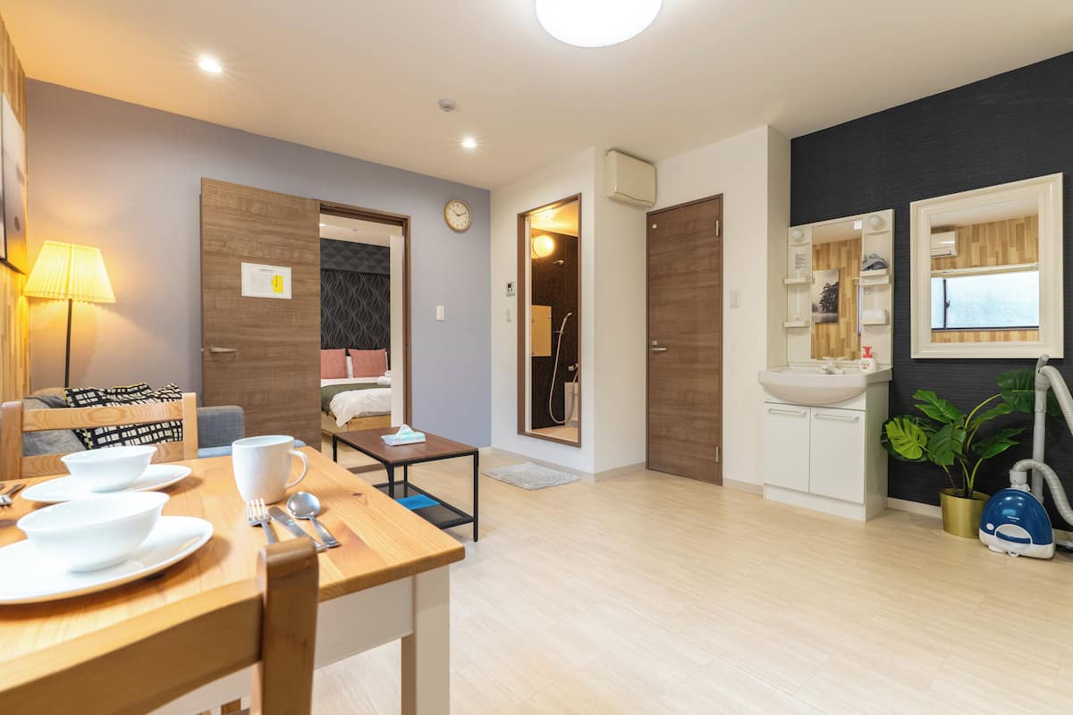 Una habitación de hotel moderna con comedor, baño con lavabo y espejo, y sala de estar con sofá y lámpara.