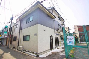 A two-story building with a beige exterior, a gated entrance, and a sign indicating a business on the ground floor. - VALUE NAMBA SOUTH  (Osaka)
