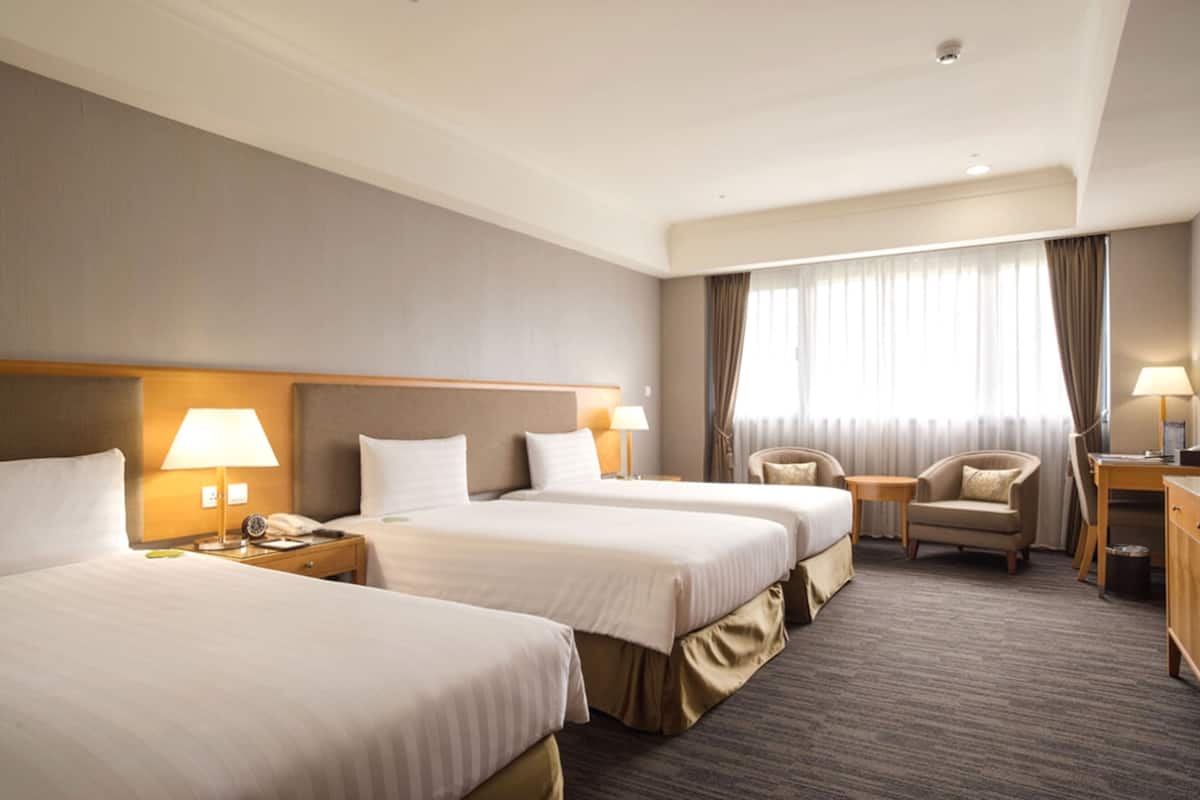 Een hotelkamer met drie bedden, een bureau, een stoel en een raam met gordijnen.
