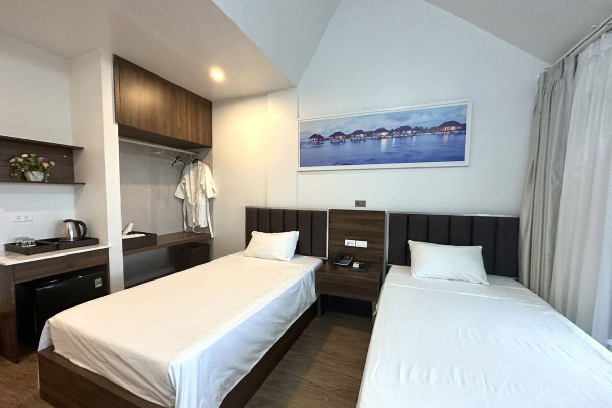 Een hotelkamer met twee bedden, een bureau, een kledingkast en een schilderij van een kustlandschap.