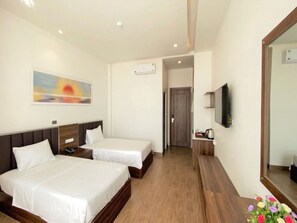 Une chambre d’hôtel avec deux lits, un tableau au mur, un climatiseur, un téléviseur fixé au mur et un plancher en bois.