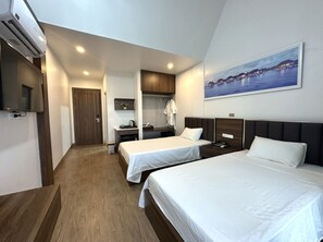 Une chambre d’hôtel avec deux lits simples, un bureau, une chaise, une petite table et un téléviseur.