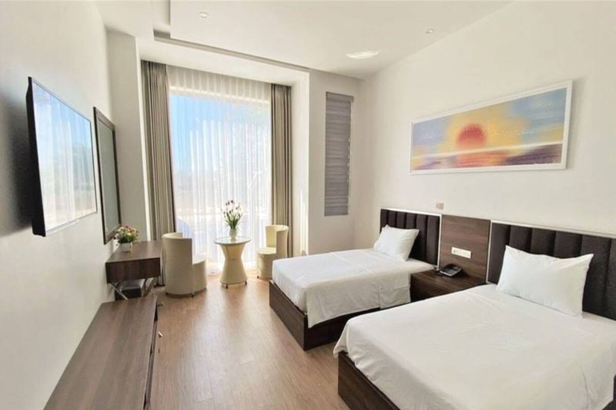Een hotelkamer met twee bedden, een bureau, een stoel, een klein tafeltje met een vaas, en een schilderij aan de muur.
