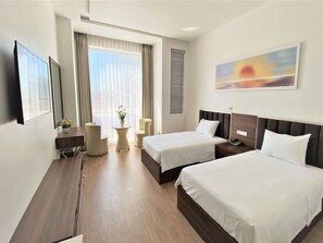 Une chambre d’hôtel avec deux lits, un bureau, une chaise, une petite table avec un vase et un tableau au mur.