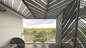 A balcony with a view of greenery and a cloudy sky. There are two wicker chairs and a small table with a cushion. - Capital O 1194 Bee Hotel (Nha Trang)