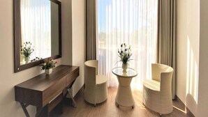 A room with a wooden console table, two wicker chairs, a glass table, and a large window with sheer curtains. - Capital O 1194 Bee Hotel (Nha Trang)
