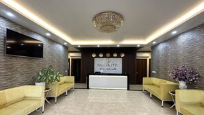 A hotel reception area with a modern design, featuring a reception desk, two yellow sofas, a potted plant, and a chandelier. - Capital O 1194 Bee Hotel (Nha Trang)