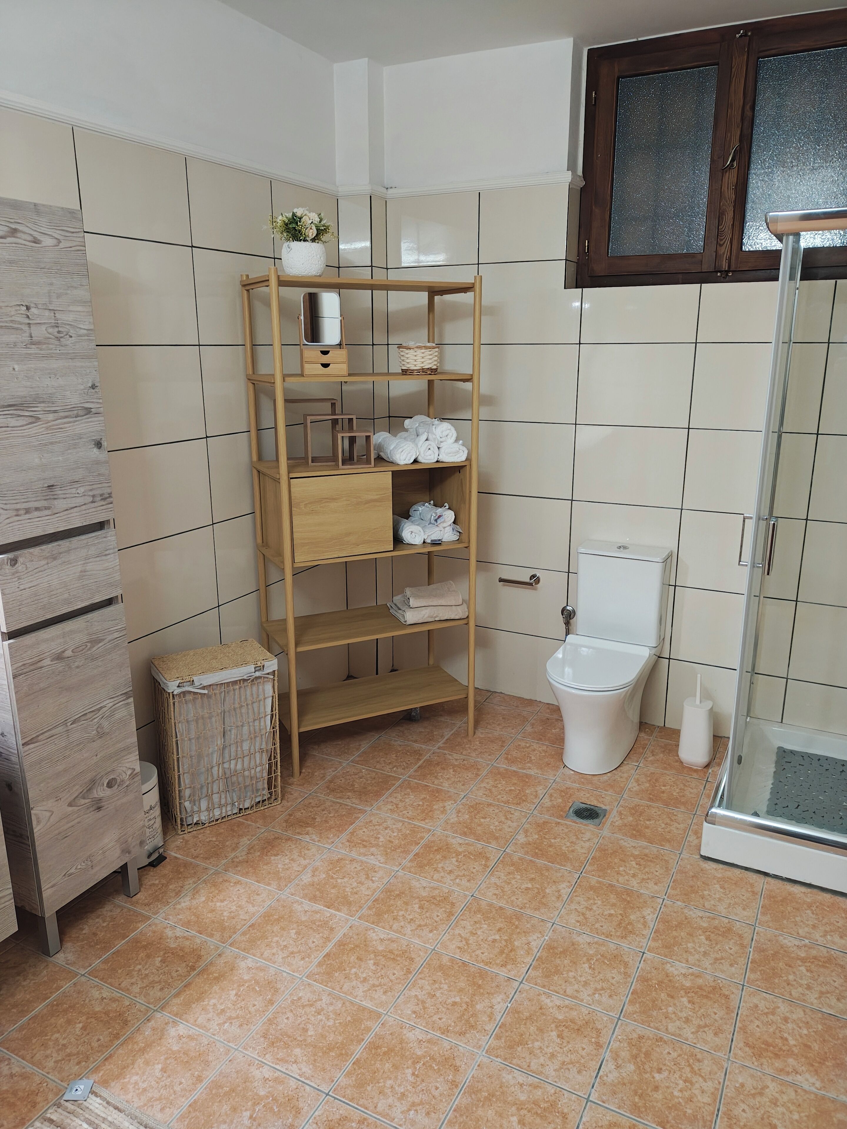 Une salle de bain comprenant un meuble-étagère en bois, des toilettes, un bidet et un espace douche.