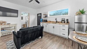 A modern kitchen with white cabinets, a black sofa, and a dining table with decorative plates. - Hidden Cottage, mins to Main St, Sleeps 4! (Fredericksburg)