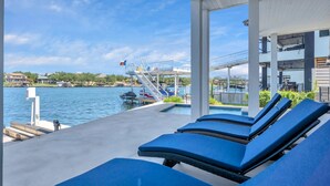 Een zwembadgedeelte met ligbedden, een duikplatform en uitzicht op het water en de omliggende gebouwen.