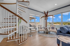 A spacious living area with a wooden staircase, a view of the sea, and nautical-themed furniture.