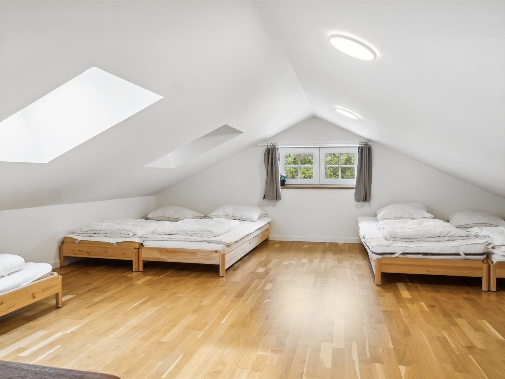 A bedroom with two beds, a skylight, and a window with curtains.