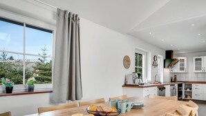 Eine moderne Küche mit Essbereich, ausgestattet mit einem Holztisch, Stühlen und Blick ins Freie.