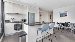 Eine moderne Küche mit weißen Schränken, einem Edelstahlkühlschrank, einer Kaffeemaschine und einem Gasherd. Es gibt einen Essbereich mit Tisch und Stühlen.