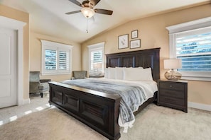 A bedroom with a dark wooden bed, a ceiling fan, a nightstand with a lamp, and a window with blinds. - Stargazer Paradise! Hot Tub, Gym & Man Cave (Monument)