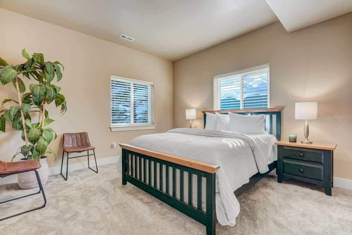 A bedroom with a bed, two bedside tables, a chair, and a potted plant.