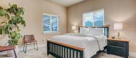 A bedroom with a bed, two bedside tables, a chair, and a potted plant.