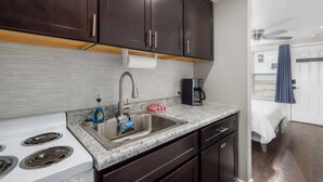 A compact kitchen with dark cabinets, a stainless steel sink, a white stove, and a countertop with a coffee maker. - Downtown Kimmswick Studio~Renovated~Prime Location (Imperial)