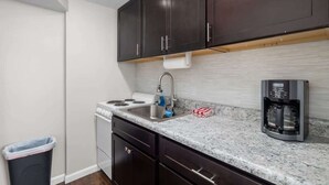 A compact kitchen with dark cabinets, a stainless steel sink, a gas stove, and a coffee maker. - Downtown Kimmswick Studio~Renovated~Prime Location (Imperial)