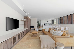 A modern living room with a flat-screen TV, a sofa, a coffee table, and a dining area with chairs.