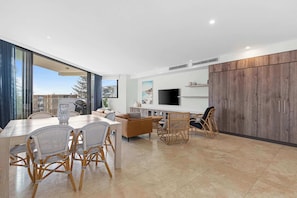 Una sala de estar moderna con comedor, televisor grande y vistas al exterior.