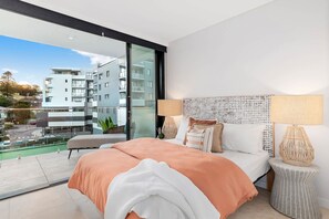 Ein modernes Schlafzimmer mit einem großen Bett, zwei Nachttischlampen und Blick auf eine Stadtkulisse durch eine Glastür.