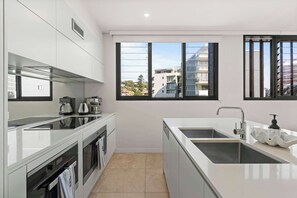 Una cocina moderna con un lavamanos doble, electrodomésticos de acero inoxidable y amplios ventanales con vistas a la ciudad.