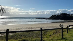 A beach with a wooden fence, grassy areas, and a distant hill with a lighthouse. - Seadream on Nelson. New listing.
Pet friendly , 300m stroll to beach and cafes.  (Woolgoolga)