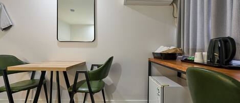Habitación de hotel pequeña con una mesa de comedor y sillas, un refrigerador compacto, una cafetera y aire acondicionado de pared.
