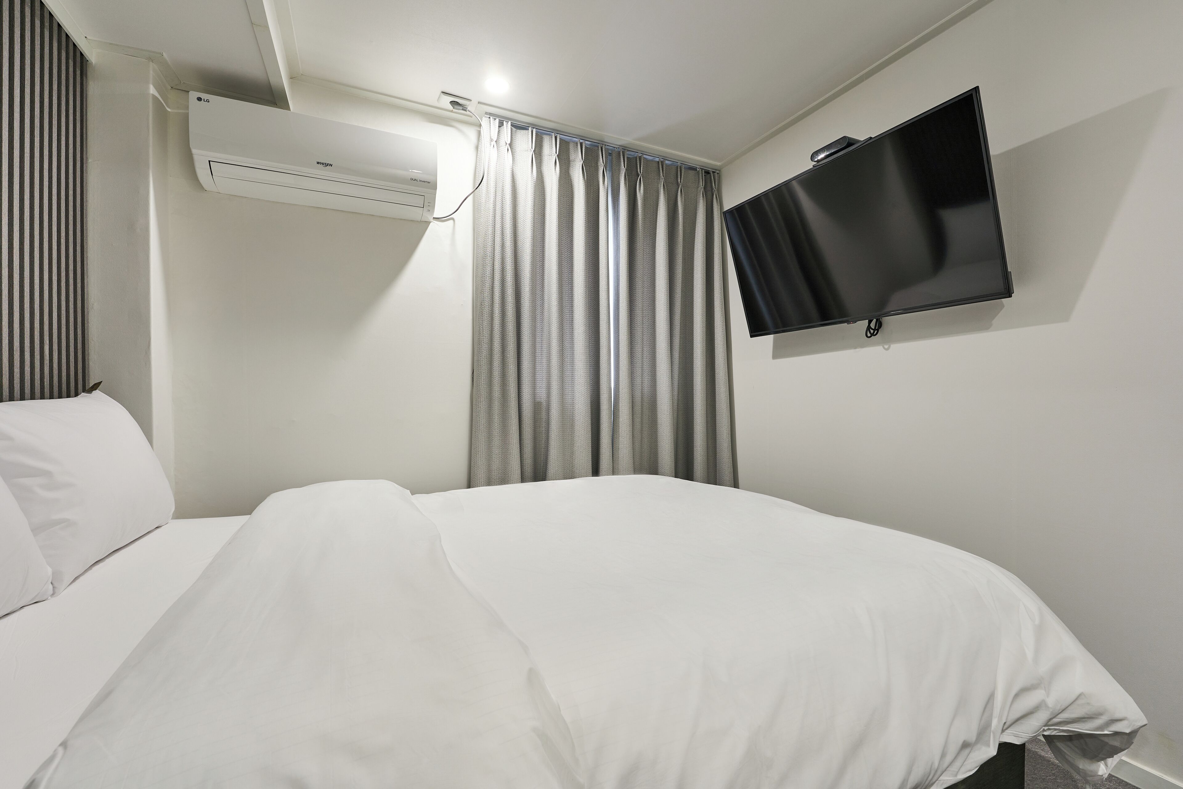 Een hotelkamer met een bed, een flatscreen-televisie aan de muur en een airconditioning.