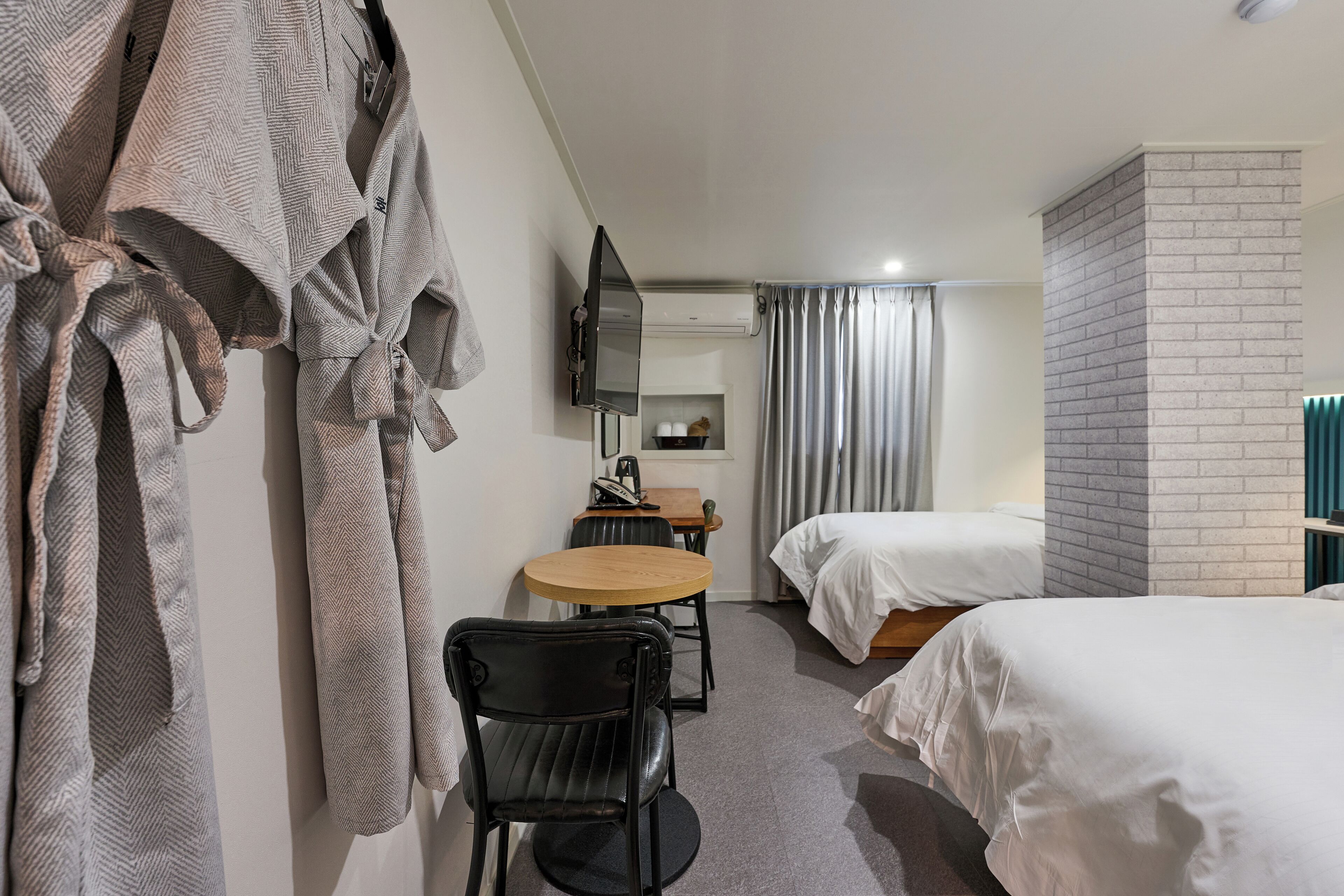 A hotel room with two beds, a desk with a chair, a TV mounted on the wall, and a brick accent wall.