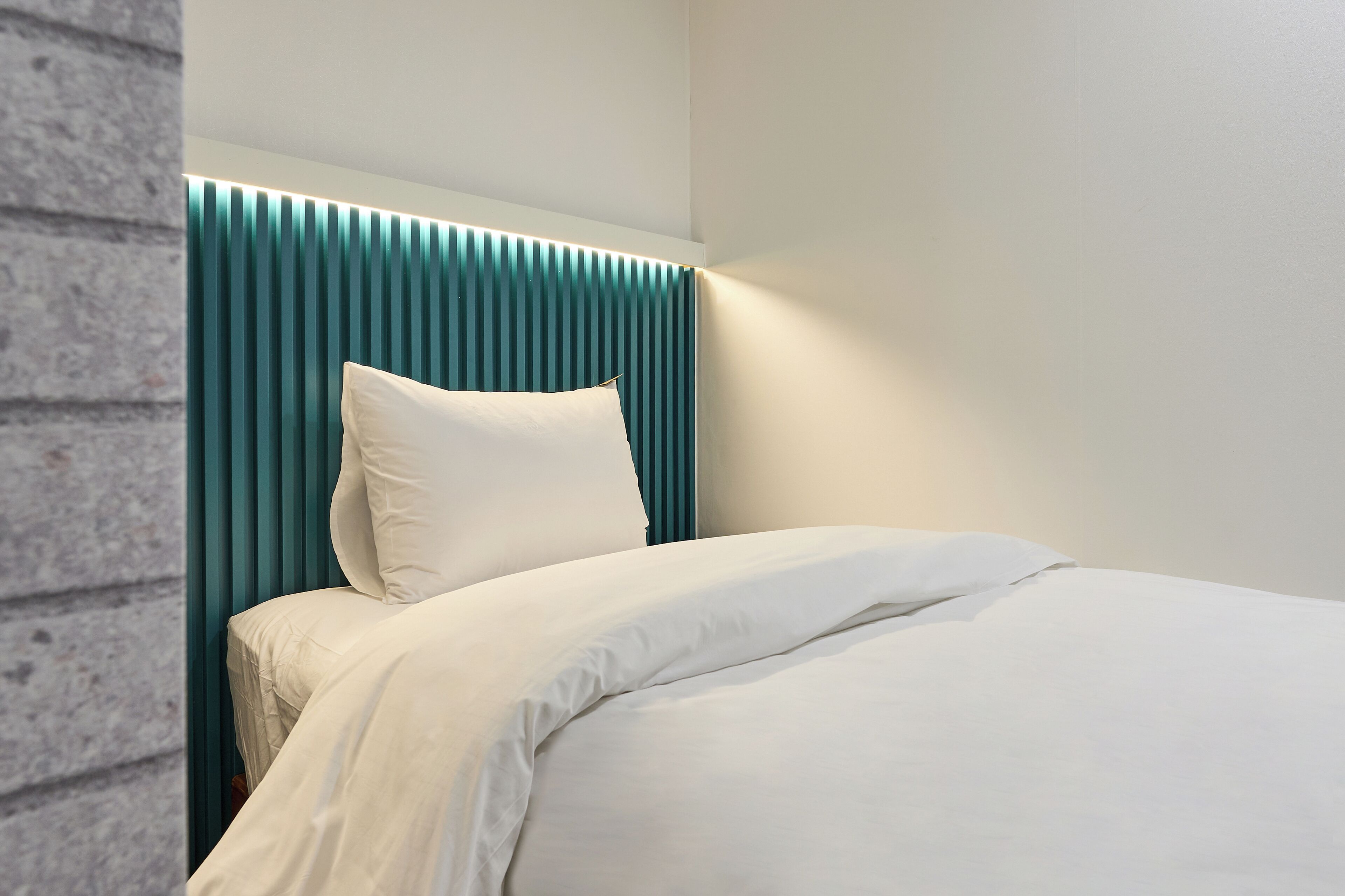 A modern bedroom with a bed, a teal headboard, and a white pillow.